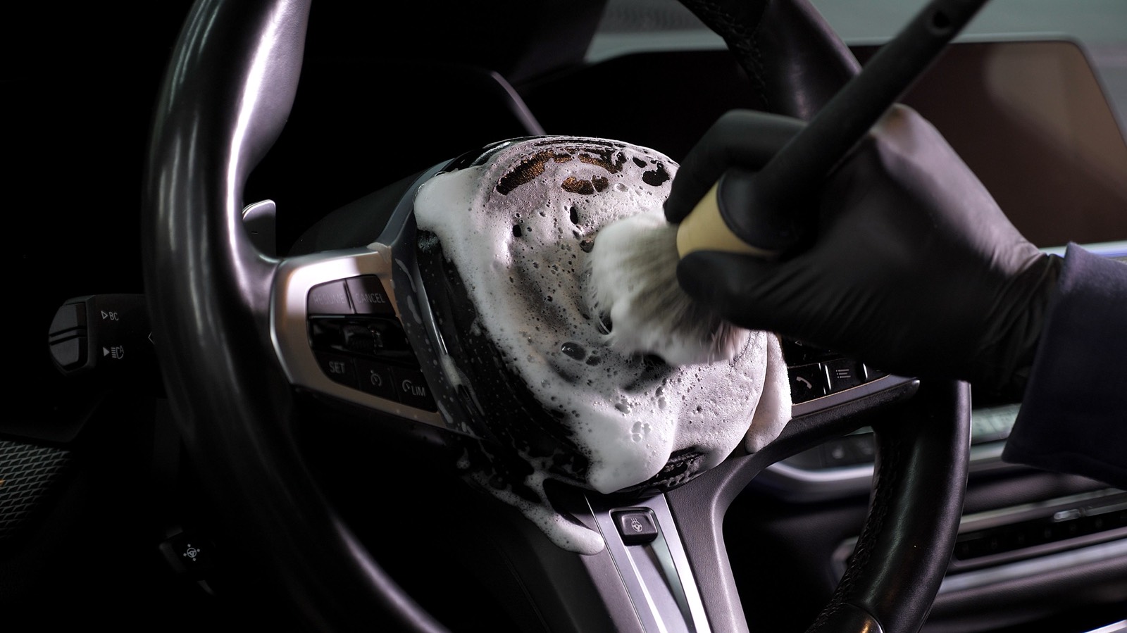 Allstar detailer cleaning a car steering wheel with foam and a detailing brush